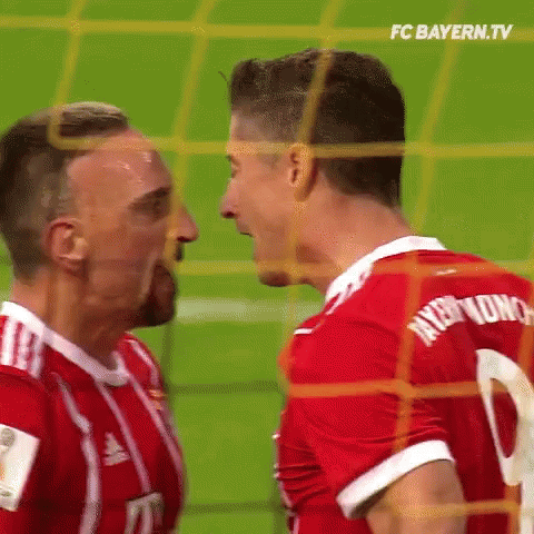 two soccer players are standing next to each other on the field and looking at each other .