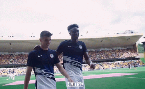 Two Soccer Players Are Walking On A Field With A Sign That Says Heitse On It GIF