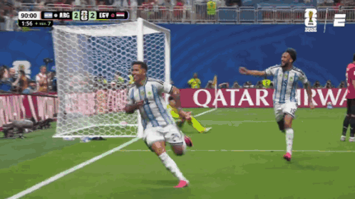 Two Soccer Players Celebrate A Goal In Front Of An Ad For Qatar GIF