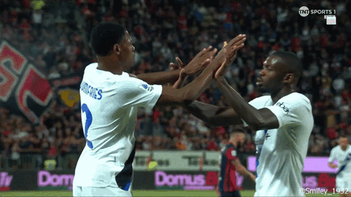 Two Soccer Players High Five in Front of Domus Banner