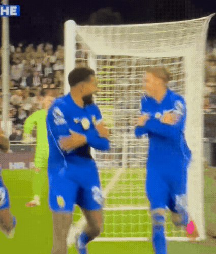 Two Soccer Players in Blue Uniforms Hugging in Front of Net Saying He