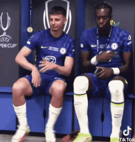 Two Soccer Players Sitting on Bench in Locker Room