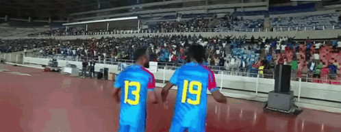 two soccer players wearing blue jerseys with the number 13 and 19 on them