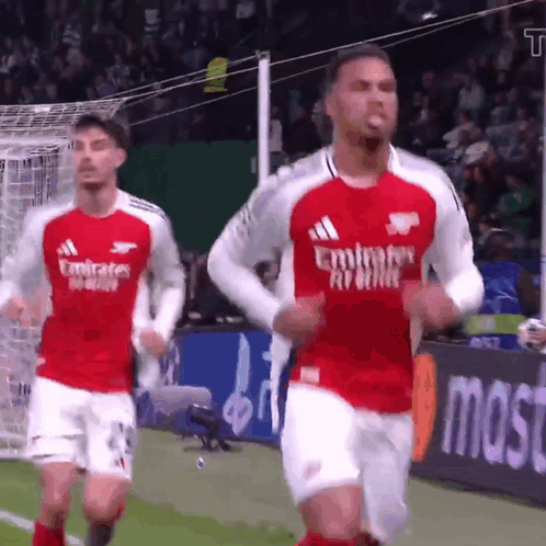 Two Soccer Players Wearing Emirates Airlines Jerseys Are Running On A Field GIF