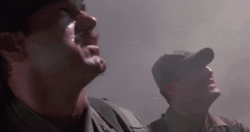 Two Soldiers Are Standing Next To Each Other In A Dark Room Looking Up At The Sky . GIF