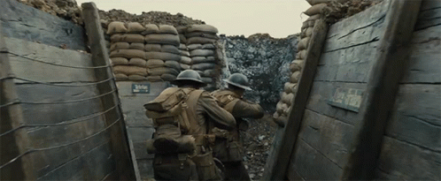 Two Soldiers Are Walking Through A Trench With A Sign That Says Clay Field On It GIF