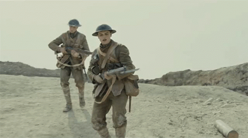 Two Soldiers Wearing Helmets And Carrying Guns Walk Across A Dirt Field GIF