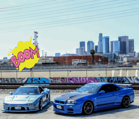 Two Sports Cars Are Parked Next To Each Other With A Boom Sign Behind Them GIF