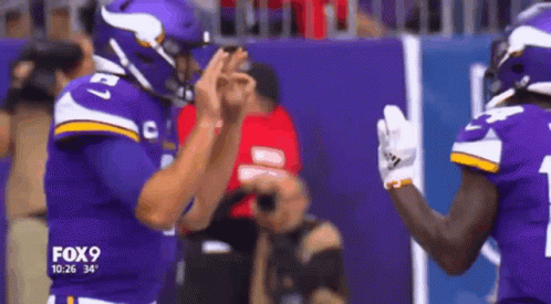 Two Vikings Football Players Are High Fiving Each Other On The Field GIF
