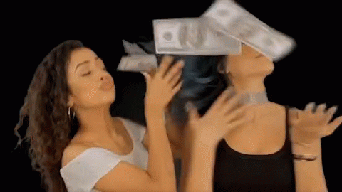 Two Women Are Blowing Money In The Air While One Of Them Has A Stack Of Money On Her Head . GIF