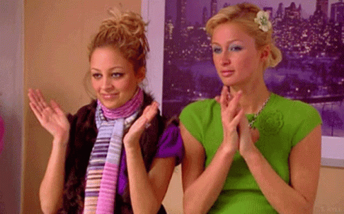 Two Women Are Clapping Their Hands In Front Of A Picture Of A City At Night . GIF