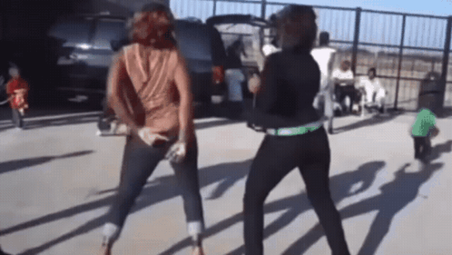 Two Women Are Dancing In A Parking Lot In Front Of A Suv GIF