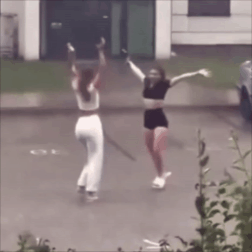 Two Women Are Dancing In A Parking Lot With Their Arms Outstretched GIF