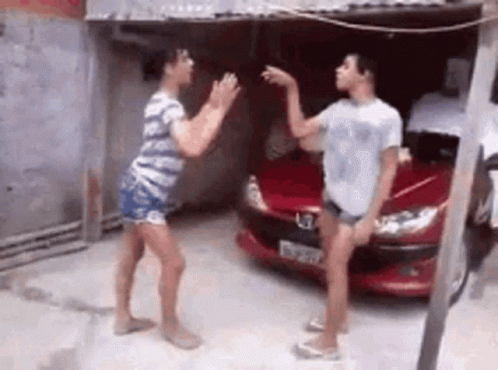 Two Women Are Dancing In Front Of A Red Car In A Parking Lot . GIF