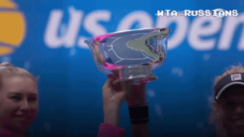 Two Women Are Holding A Trophy In Front Of A Sign That Says Us Open GIF