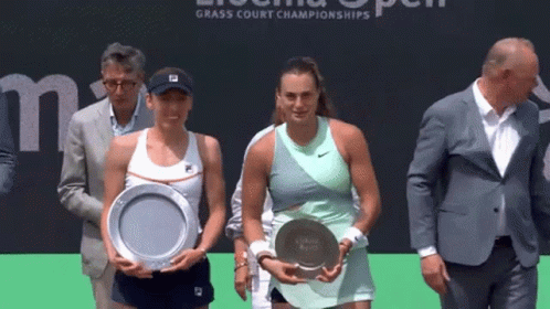 two women are holding trophies in front of a sign that says grass court championships .