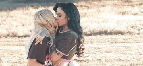 Two Women Are Kissing In A Field While Standing Next To Each Other . GIF