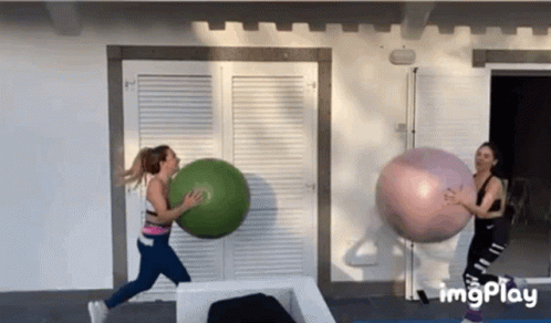 Two Women Are Playing With Giant Exercise Balls In Front Of A Building . GIF