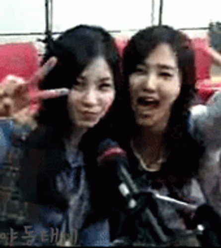 Two Women Are Posing For A Picture And One Is Making A Peace Sign GIF