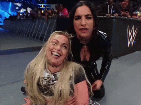 Two Women Are Posing For A Picture In Front Of A Sign That Says W GIF