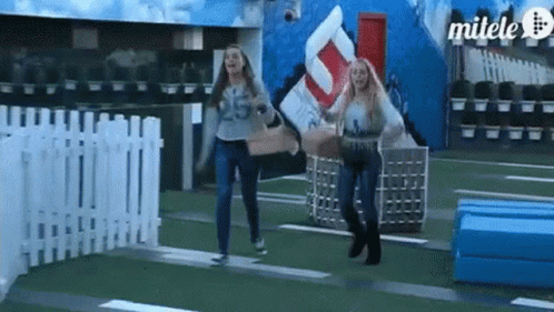 Two Women Are Running In Front Of A Sign That Says Milele GIF