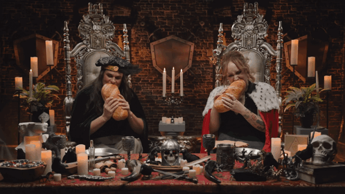 Two Women Are Sitting At A Table Eating Bread And Drinking Wine GIF