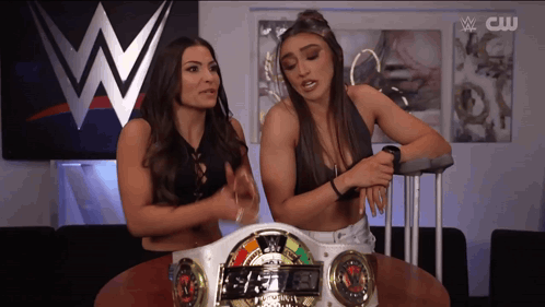 two women are sitting at a table in front of a wwe sign