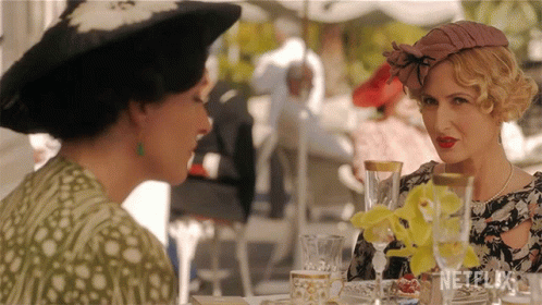 Two Women Are Sitting At A Table With Netflix Written On The Bottom GIF