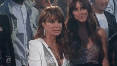 Two Women Are Sitting In A Crowd And One Is Wearing A White Jacket . GIF