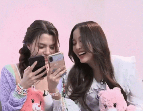two women are sitting next to each other and looking at their phones .