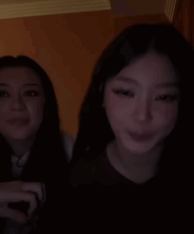 Two Women Are Sitting Next To Each Other In A Dark Room And Smiling . GIF