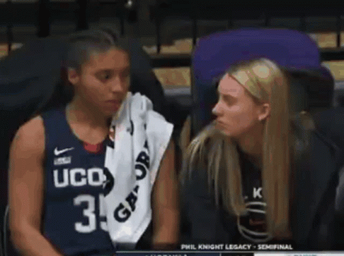 Two Women Are Sitting Next To Each Other In A Stadium . One Of The Women Is Wearing A Ucd Jersey . GIF