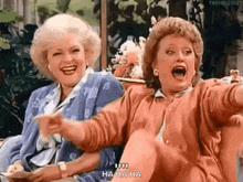 Two Women Are Sitting Next To Each Other Laughing And Pointing At Something . GIF