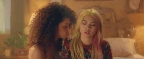 Two Women Are Sitting Next To Each Other On A Bed . One Of The Women Has Pink Hair . GIF