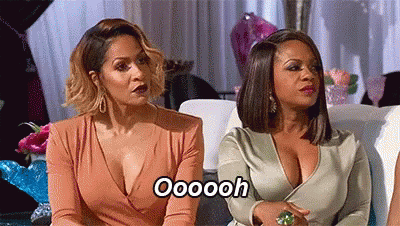 Two Women Are Sitting Next To Each Other On A Couch And One Of Them Is Wearing A Plunging Neckline Dress . GIF
