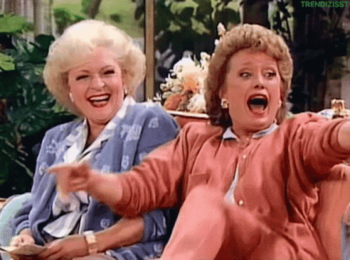 Two Women Are Sitting Next To Each Other On A Couch Laughing And Pointing . GIF