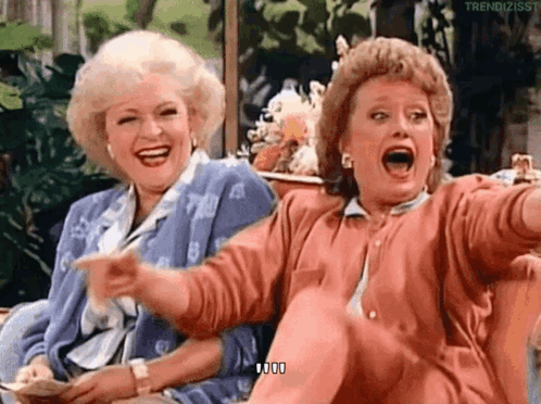 Two Women Are Sitting Next To Each Other On A Couch Laughing And Pointing . GIF