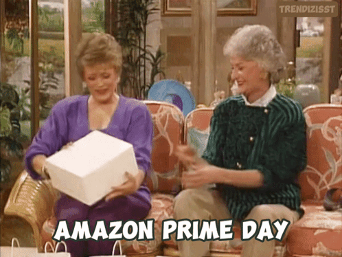 Two Women Are Sitting On A Couch And One Of Them Is Holding An Amazon Prime Day Gift GIF