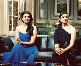 Two Women Are Sitting On A Couch One In A Blue Dress And One In A Black Dress GIF