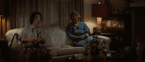 Two Women Are Sitting On A Couch One Is Knitting The Other Is Drinking Tea GIF