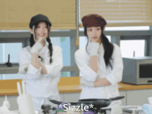 Two Women Are Standing In A Kitchen And The Word Sizzle Is On The Bottom Left GIF