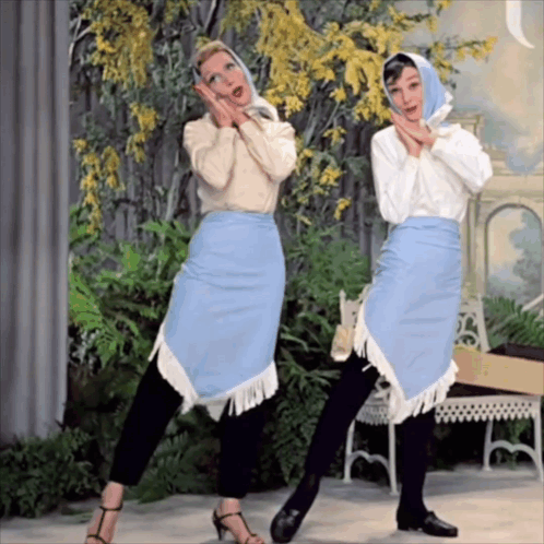 Two Women Are Standing Next To Each Other And One Is Wearing A Blue Skirt With Fringe GIF