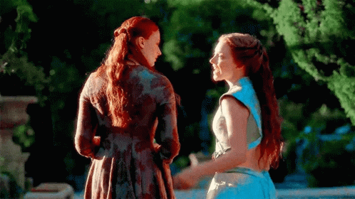 Two Women Are Standing Next To Each Other Holding Hands In A Garden . GIF