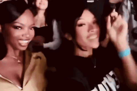 two women are standing next to each other in a crowd at a party and smiling .