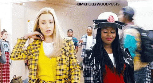 Two Women Are Standing Next To Each Other In A Hallway . One Of The Women Is Wearing A Yellow Plaid Shirt . GIF