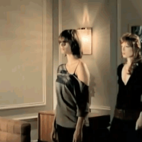Two Women Are Standing Next To Each Other In A Living Room In Front Of A Wall . GIF