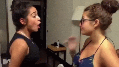 two women are standing next to each other in a room and having a fight .
