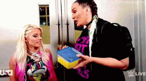 two women are standing next to each other in a room and one is holding a lunch box .
