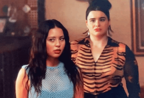 Two Women Are Standing Next To Each Other In A Room . One Of The Women Is Wearing A Tiger Print Shirt . GIF