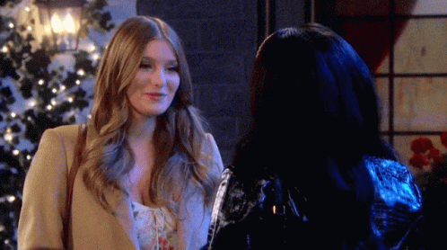 Two Women Are Standing Next To Each Other In Front Of A Christmas Tree And Smiling GIF